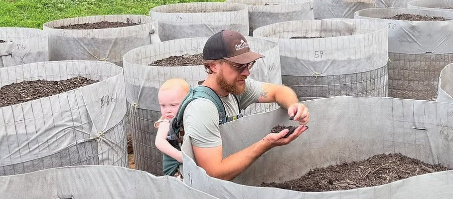 Everest Holmes and child working with soil in large gray containers on a farm.
